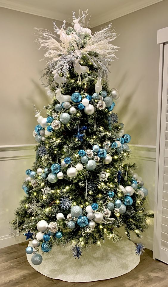 a chic Christmas tree with blue, silver and white ornaments, snowflakes, lights and white branches and deer on top