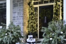 a chic black and white Christmas porch with mini Christmas trees and lights, a garland, snowy arrangement and candle lanterns