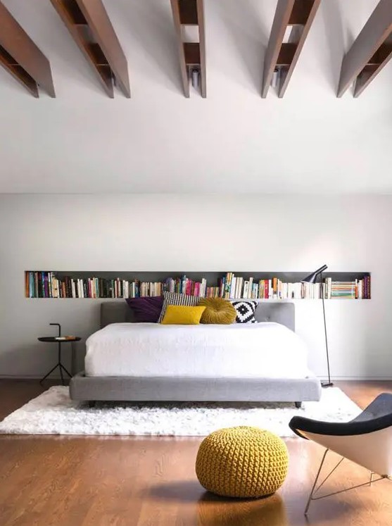 a contemporary bedroom with a long niche shelf, a bed with bold pillows, a black side table and black chair