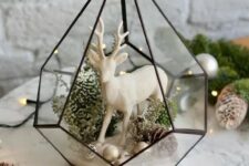 a cool and stylish Christmas terrarium with small ornaments, pinecones, moss and greenery and a white deer