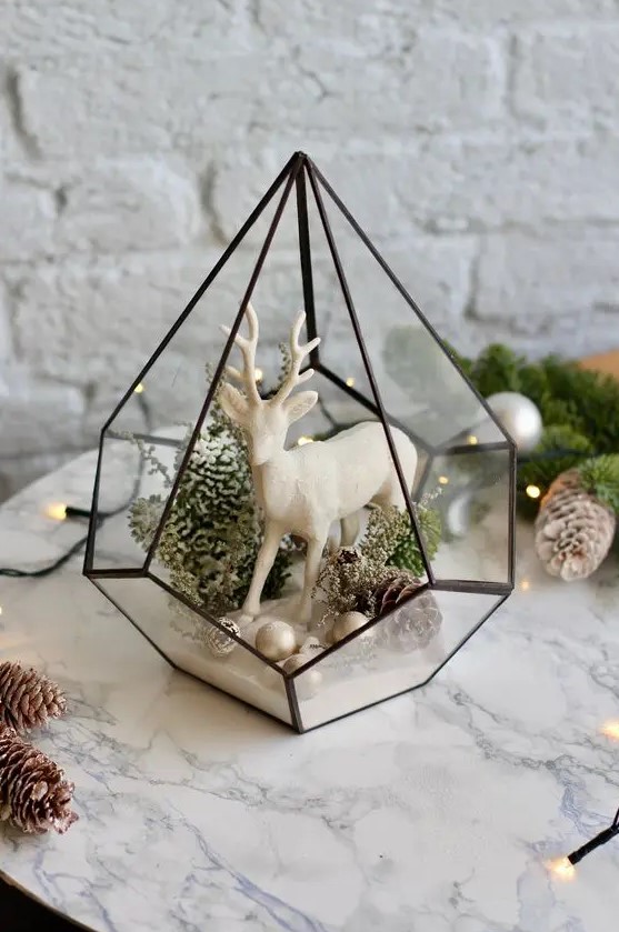 a cool and stylish Christmas terrarium with small ornaments, pinecones, moss and greenery and a white deer