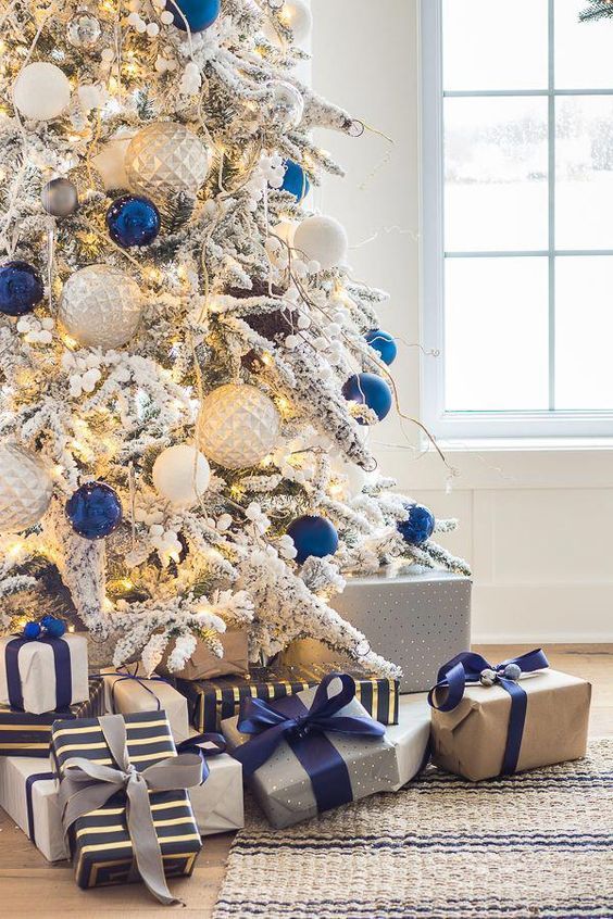 a cool flocked Christmas tree with white, silver and navy ornaments that make a statement and create a contrast, with berries and piles of gifts