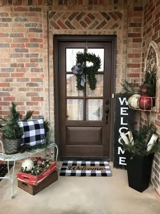 a cozy farmhouse Christmas porch with plaid linens, evergreens, bells and ornaments feels vintahe and rustic and invites in