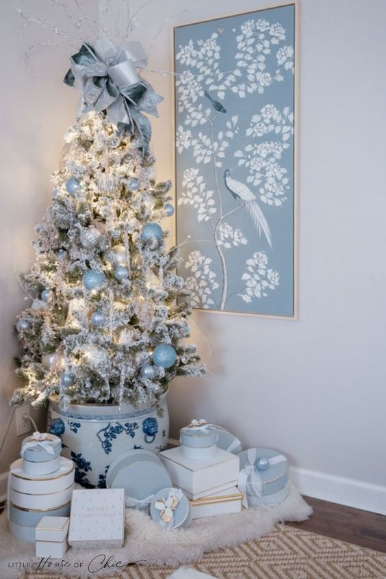 a flocked Christmas tree in a planter, with pearly, silver and pastel blue ornaments, a pastel blue bow on top and some lights