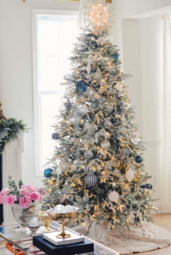 a flocked Christmas tree with lights, white, silver and bold blue ornaments, poinsettias and beads is a gorgeous decoration