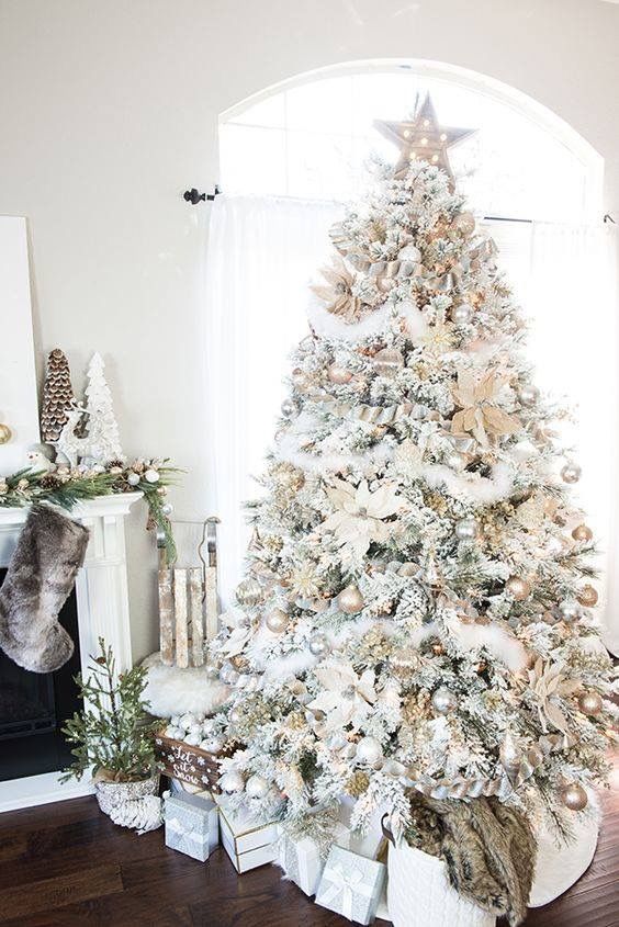 a flocked Christmas tree with white, gold and silver ornaments, ribbons, faux blooms, faux snow garlands and lights