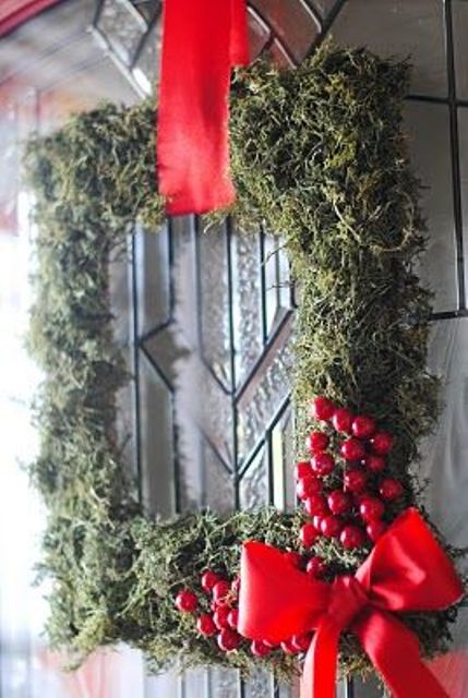 a frame Christmas wreath covered with moss, berries, a large red bow and a red ribbon on top is amazing