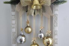 a frame Christmas wreath with a gold star, evergreens, silver and gold ornaments, burlap and a ribbon bow plus a bell