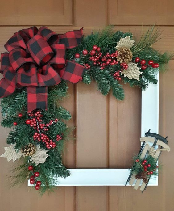 a frame Christmas wreath with evergreens, berries, pinecones and felt leaves plus a large plaid bow and a sleight on the corner