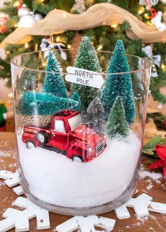 a fun Christmas terrarium in a large jar, with faux snow, a red van, some bottle brush Christmas trees