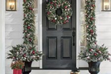 a glam Christmas porch styled with an evergreen garland with white and red ornaments, a matching wreath and arrangements in pots plus red rubber boots