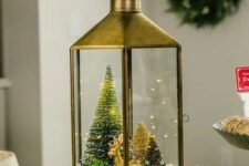 a lantern Christmas terrarium with faux snow, a gold deer, bottle brush trees and some greenery is a chic solution