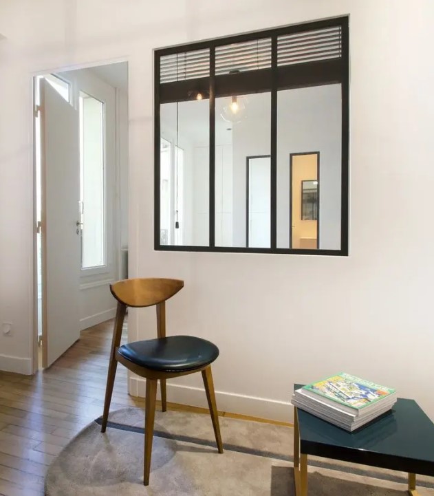 a living room is connected to the next space with a window with a black frame looks stylish and lets light in