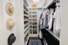 a long and narrow walk-in closet in white, with lots of shoe shelves, open storage and just some boxes on top plus hat holders