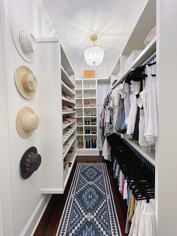 a long and narrow walk-in closet in white, with lots of shoe shelves, open storage and just some boxes on top plus hat holders