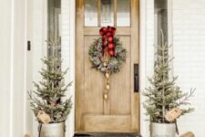 a lovely Christmas porch with a plaid rug and a flocked Christmas wreath with a plaid bow and bells, potted Christmas trees and wooden deer