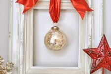 a mini Christmas wreath of a white frame, a single mercury glass ornament and a large red ribbon bow on top