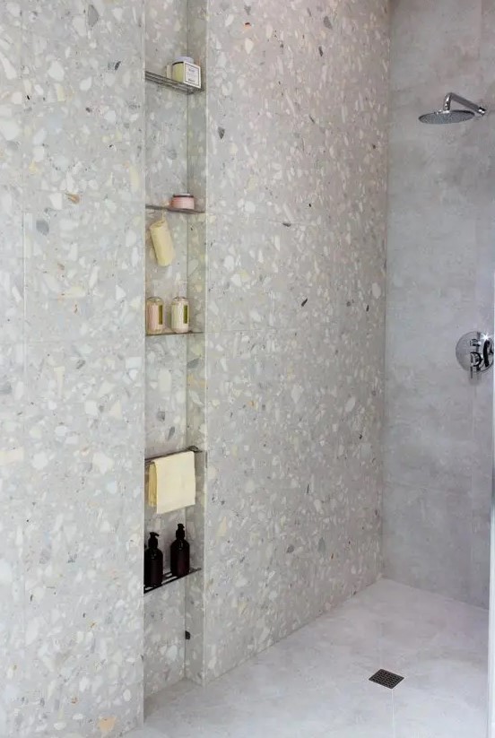 a minimalist shower space clad with stone tiles and with a long and narrow niche with metal shelves is a cool nook