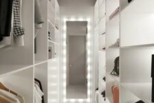 a minimalist white closet with shelves and open storage compartments, with a lit up mirror and lit up shelves is cool and features a lot of space