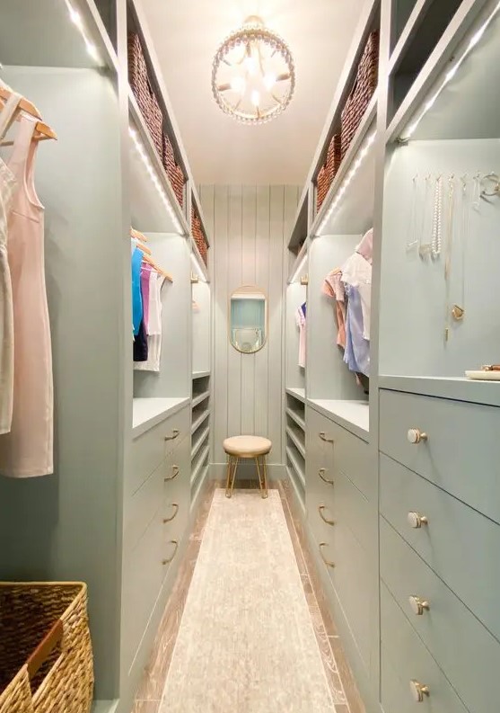 a mint green narrow closet with lots of drawers and open storage compartments, with lit up shelves and a chandelier