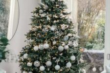 a modern Christmas tree styled with white, silver and clear ornaments and with lights and snowflakes is a chic idea