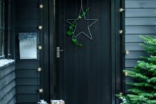 a moody Christmas porch with a Christmas tree, firewood in a metal holder, a sleigh with gift boxes and a star wreath on the door