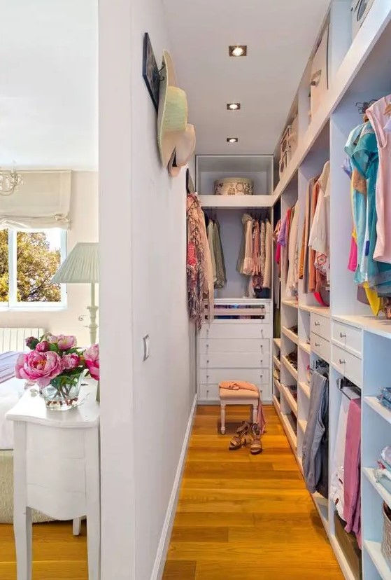 a narrow closet with open storage compartments, drawers, railings and lights, a har organizer hanging on the wall