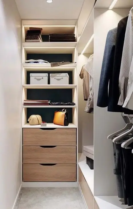 a narrow white closet with lit up open storage compartments, railing and a built-in dresser is a stylish and cool space