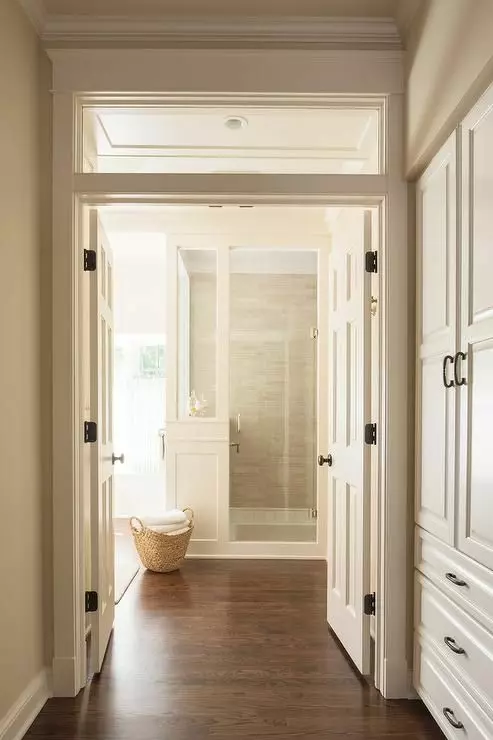 a neutral corridor and a bathroom with double doors and a transom window that brings some light from bathroom windows to the corridor