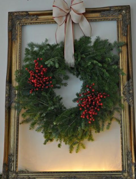 a pretty Christmas decoration - a lush evergreen and berry wreath with a neutral bow attached to an oversized gilded frame
