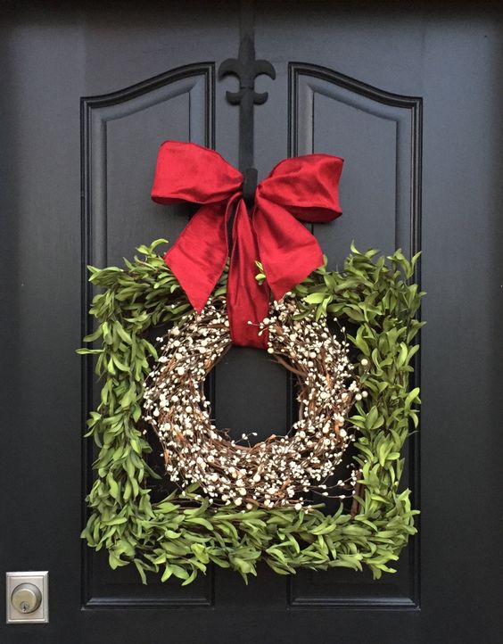 a pretty frame Christmas wreath covered with greenery and with a blooming wreath inside plus a large red bow on top