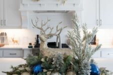 a pretty table Christmas decoration of evergreens, leaves, silver, copper and bold blue ornaments, silver pinecones and a large deer