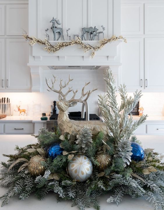 a pretty table Christmas decoration of evergreens, leaves, silver, copper and bold blue ornaments, silver pinecones and a large deer
