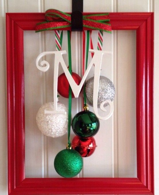a red frame Christmas wreath with white, silver, green and red ornaments and bells, a matching bow and a monogram