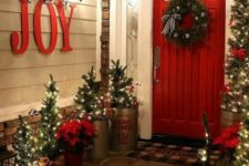 a rustic Christmas porch with lots of trees in pots, poinsettias, a wreath and JOY letters is a very festive space