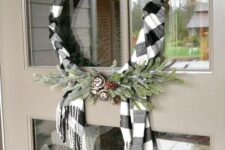a rustic Christmas wreath with a buffalo check scarf, evergreens, bells and pinecones is a cool and cozy decor idea