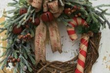 a rustic Christmas wreath with a burlap bow, bells, berries, a large candy cane and evergreens is a cozy and lovely idea