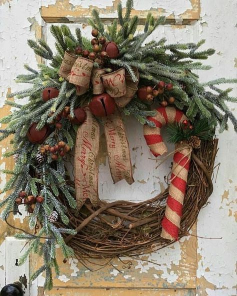 a rustic Christmas wreath with a burlap bow, bells, berries, a large candy cane and evergreens is a cozy and lovely idea