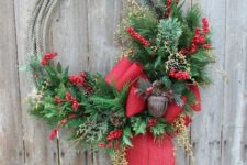 a rustic Christmas wreath with evergreens, berries, a red burlap bow, a nut is a lovely decor idea for a rustic space