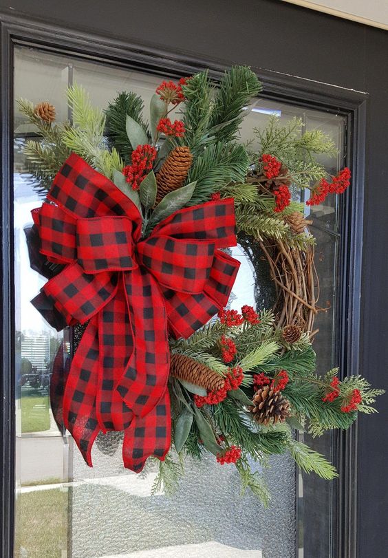 a rustic Christmas wreath with evergreens, red berries, pinecones and a red plaid bow is a lovely decoration to rock