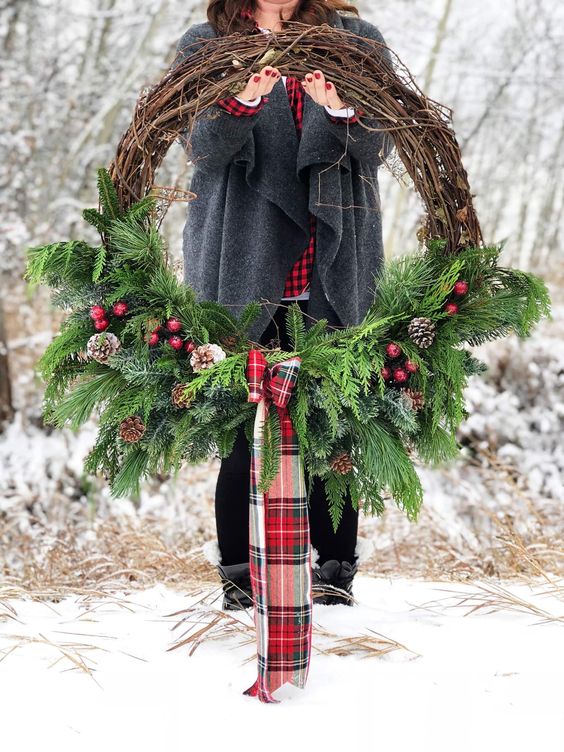 a rustic Christmas wreath with evergreens, snowy pinecones, red berries and a red plaid bow is a lovely decoration to make