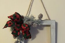 a rustic frame Christmas wreath with a red faux bird, a plaid bow, bleached pinecones and evergreens is all cool