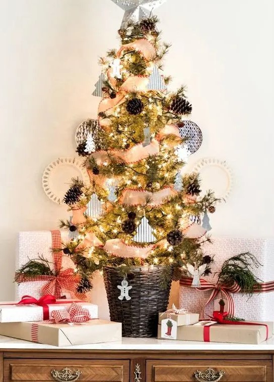 a rustic tabletop Christmas tree with lights, pinecones, little paper and clay ornaments and a basket as a base