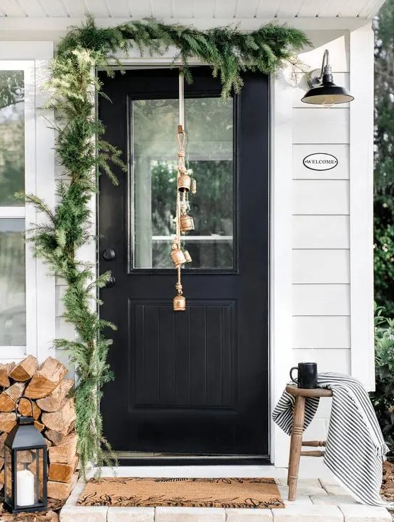 a simple and natural Christmas porch with evergreens, firewood, candle lanterns and bells on the door is very cool