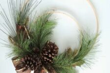 a simple rustic Christmas wreath of two embroidery hoops, evergreens, pinecones and a printed ribbon bow is cool