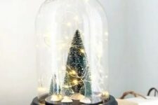 a small and cute Christmas terrarium with bottle brush Christmas trees and lights is a cool decor idea
