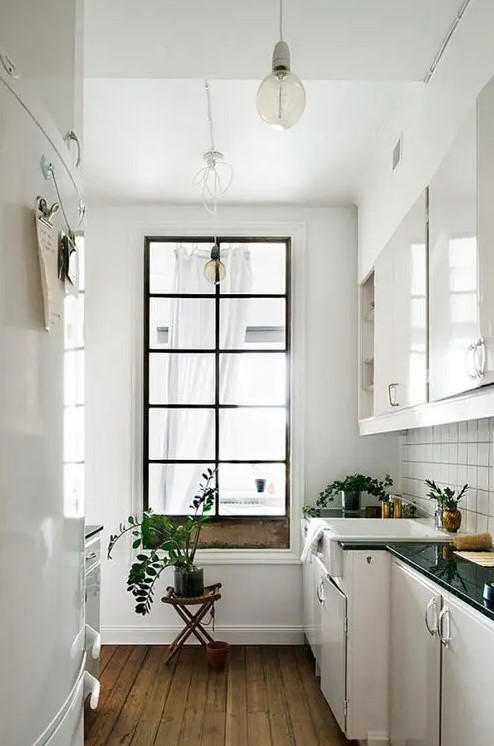 a small kitchen features a tall window to the living room that gives natural light to the space and makes it look bigger