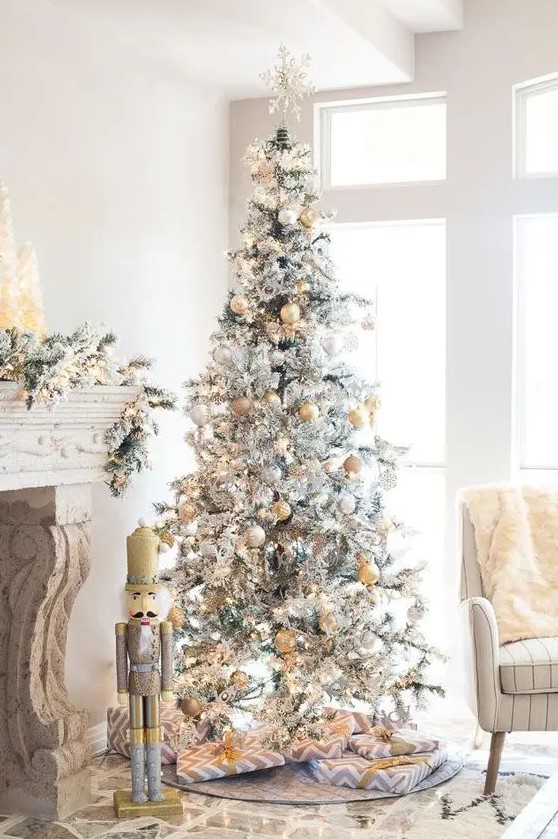 a snowy Christmas tree with gold and silver ornaments and a snowflake on top looks glam