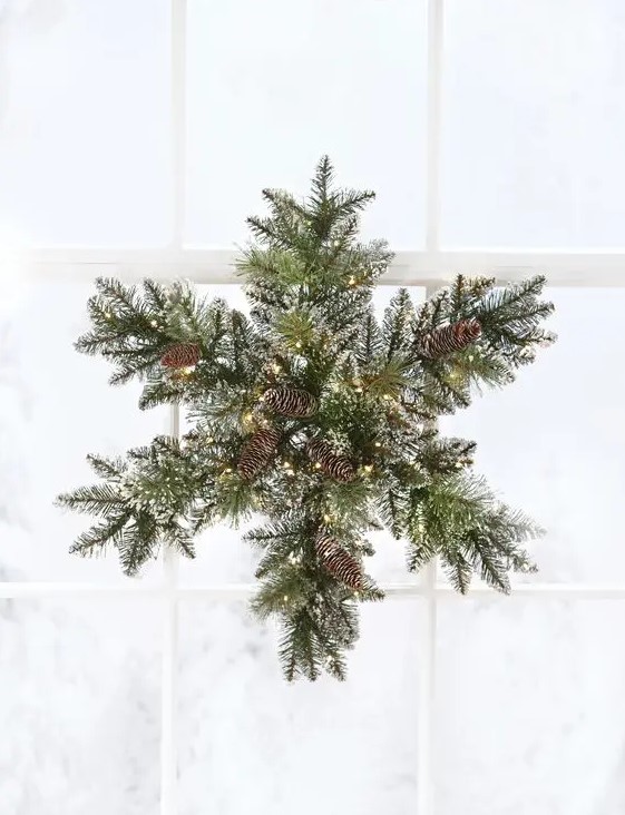 a snowy evergreen Christmas wreath with pinecones and lights shaped as a snowflake
