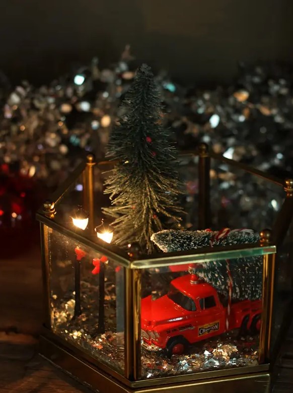 a stylish Christmas terrarium with gold glitter, a red truck with a Christmas tree and some street lamps plus one more tree